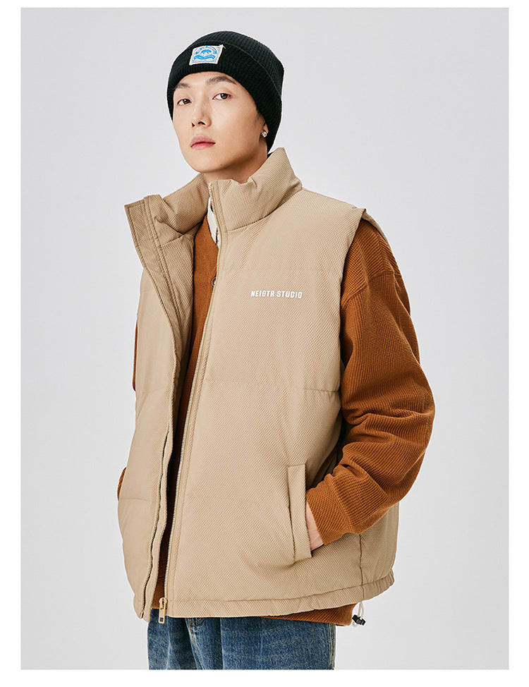 Man wearing tan quilted vest with brown corduroy sleeves, black beanie with mountain logo and NEIGTR STUDIO branding against white background