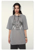 Model wearing gray oversized t-shirt with "BRAVE ABLE" tiger graphic design, silver headphones, chain necklace and watch against white background
