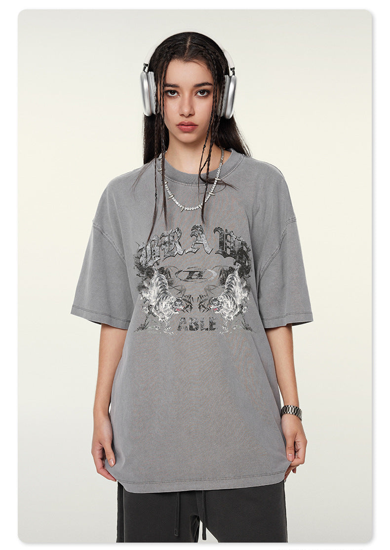 Model wearing gray oversized t-shirt with "BRAVE ABLE" tiger graphic design, silver headphones, chain necklace and watch against white background