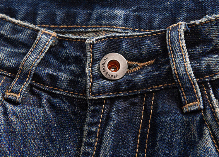 A closeup of indigo jeans showing the metal button closure with 'JEANS FASHION' engraving on the waistband