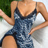 A model wearing blue leopard print satin slip dress with black lace trim, posing with plants visible in background