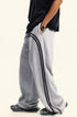 Side profile of model wearing black t-shirt with gray track pants featuring black side stripes, silver watch visible on wrist against beige background