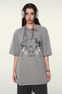 A model with dark hair wearing silver headphones, a gray oversized t-shirt featuring "BRAVE ABLE" graphic with tiger designs, silver chain necklace