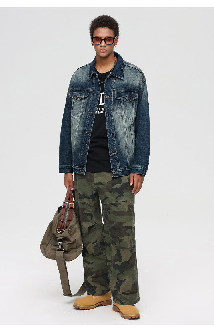 Full-length shot of male model in denim jacket, camo pants, and boots with duffle bag