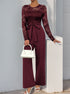 A burgundy version of the lace jumpsuit, styled with white heels and a handbag against a neutral background.