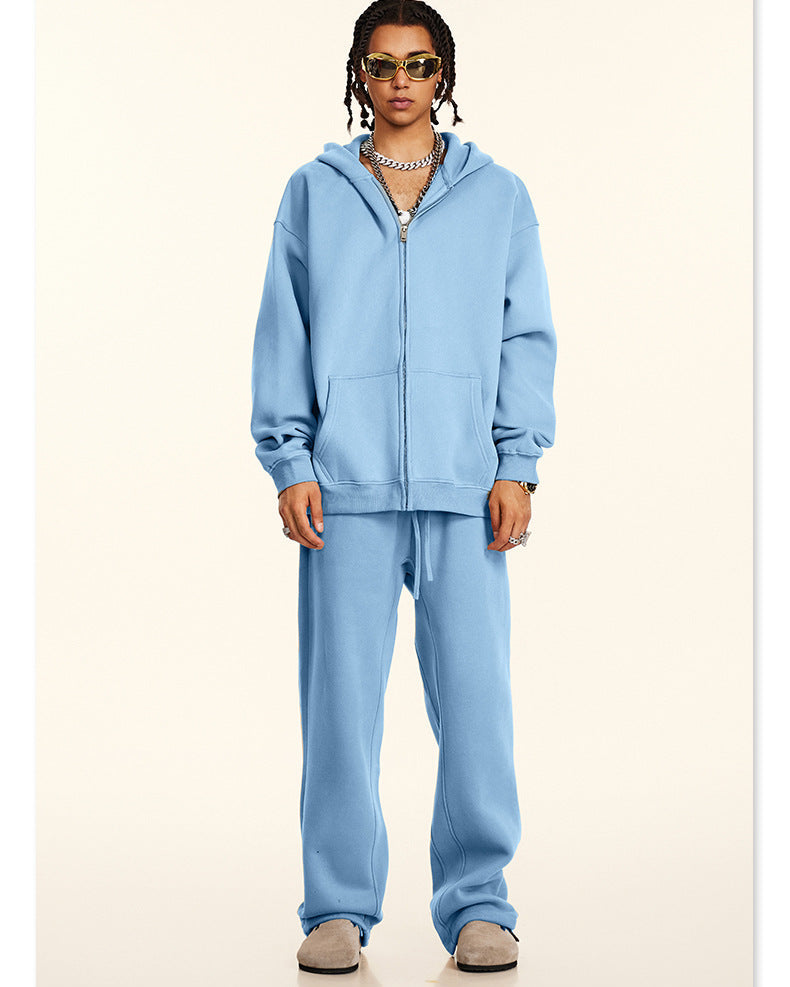 Model wearing oversized light blue zip-up hoodie and matching sweatpants with gold-framed sunglasses and layered silver chain necklaces against cream background