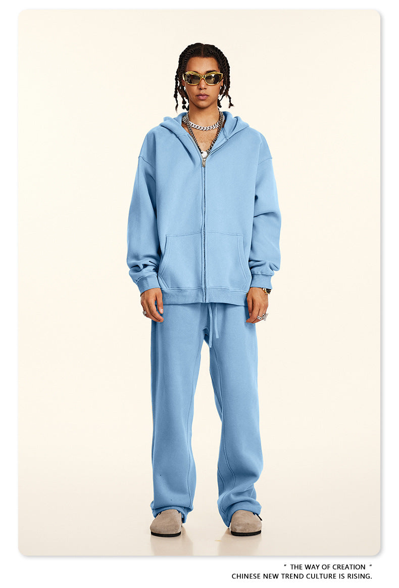 Model wearing oversized light blue zip-up hoodie and matching sweatpants with gold-framed sunglasses and layered silver chain necklaces against cream background