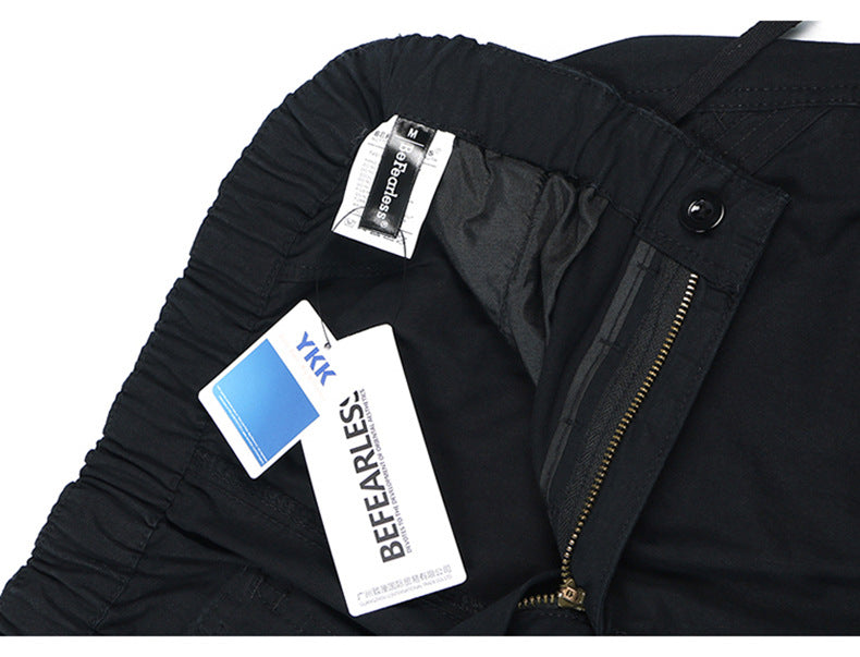 Detail of black cargo pants waistband showing zipper closure, size tag, and BEFEELESS brand label on white background