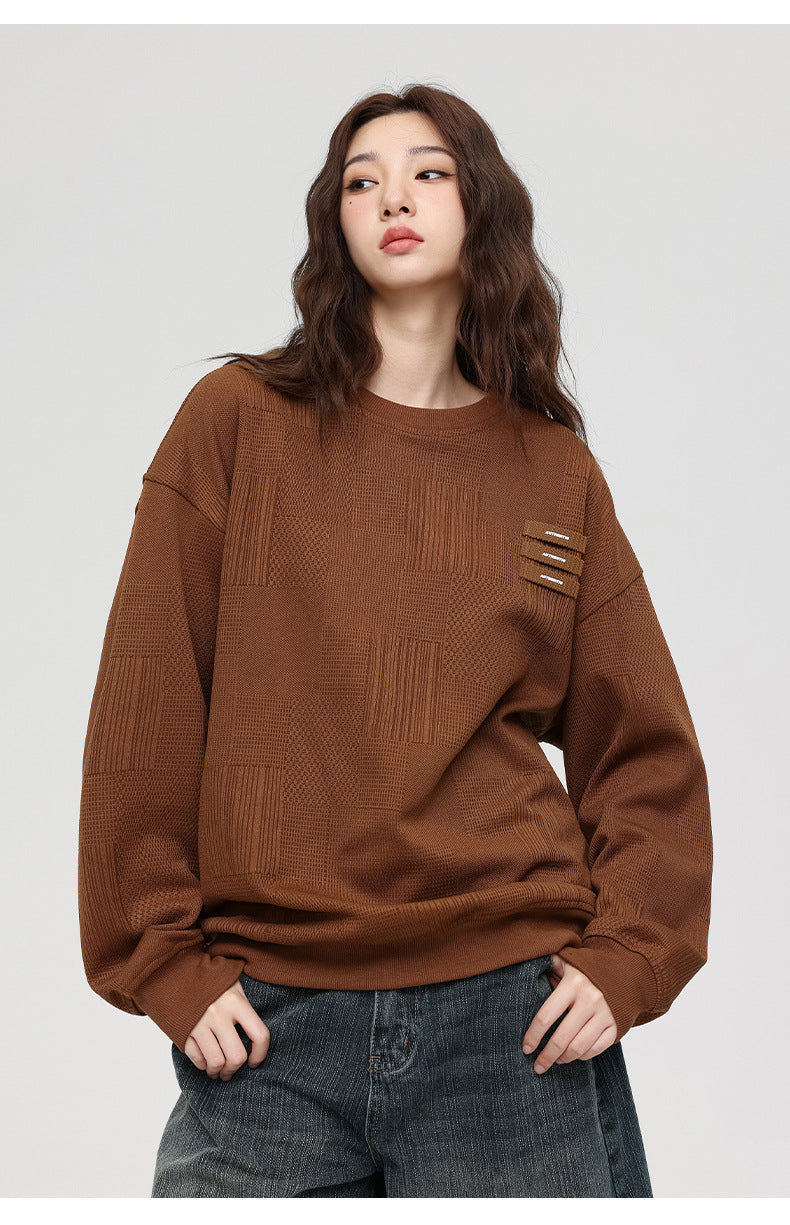 Woman with wavy brown hair looking to side, wearing brown textured sweatshirt and denim culottes