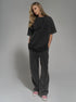 Woman wearing a black oversized t-shirt and dark gray pants on a plain background