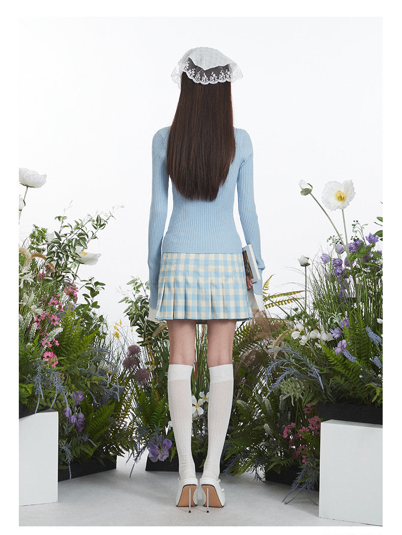 Back view showing slim-fit blue sweater and pleated gingham mini skirt, highlighting the skirt's A-line silhouette and white knee sock styling.