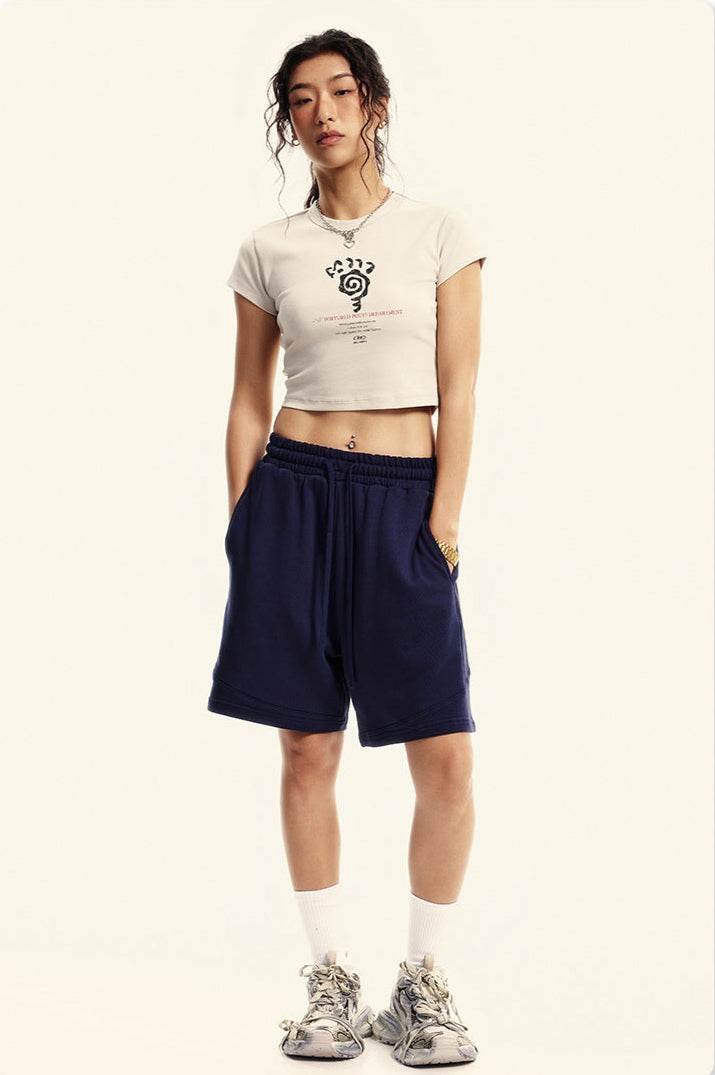 Model in a white cropped T-shirt with a graphic design, navy sweat shorts, white socks, and sneakers