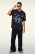 A model adjusting white sunglasses while wearing black graphic t-shirt with blue 'B' logo, silver chain necklace and black pants