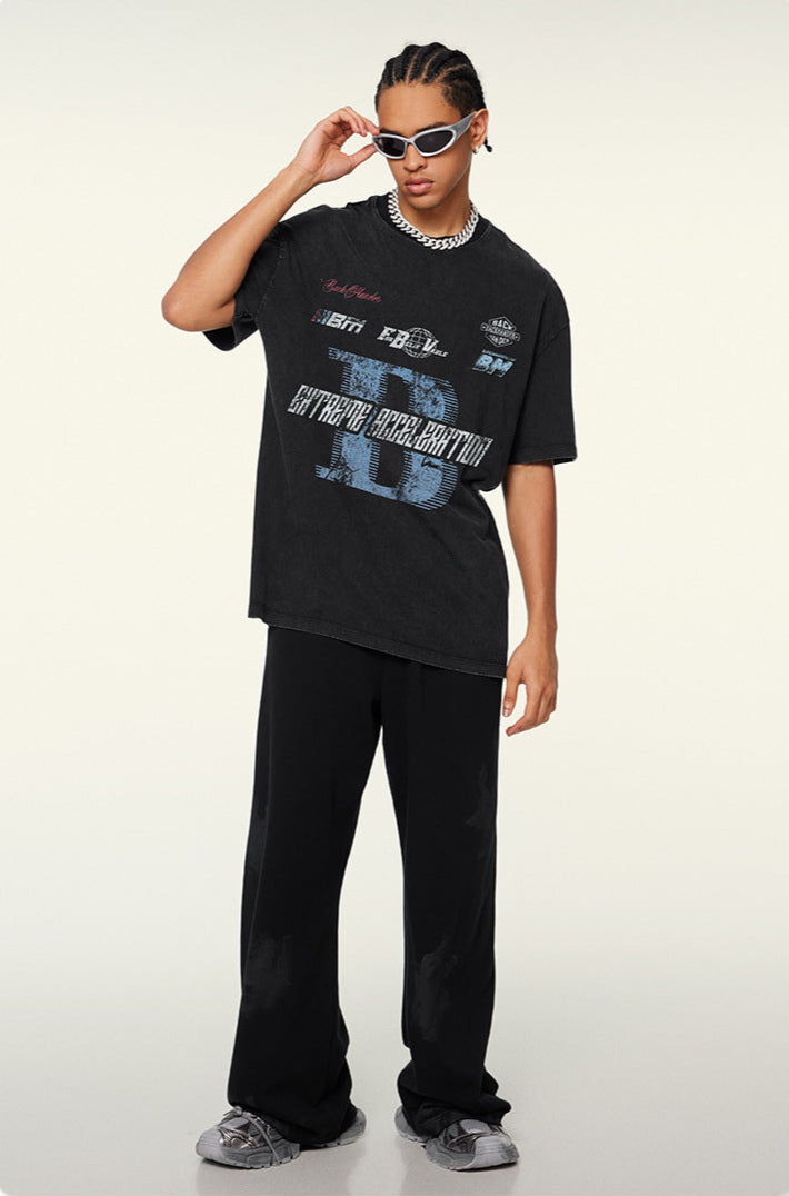 A model adjusting white sunglasses while wearing black graphic t-shirt with blue 'B' logo, silver chain necklace and black pants