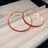 A pair of small gold hoop earrings with red enamel and decorative accents, placed on a white ceramic plate