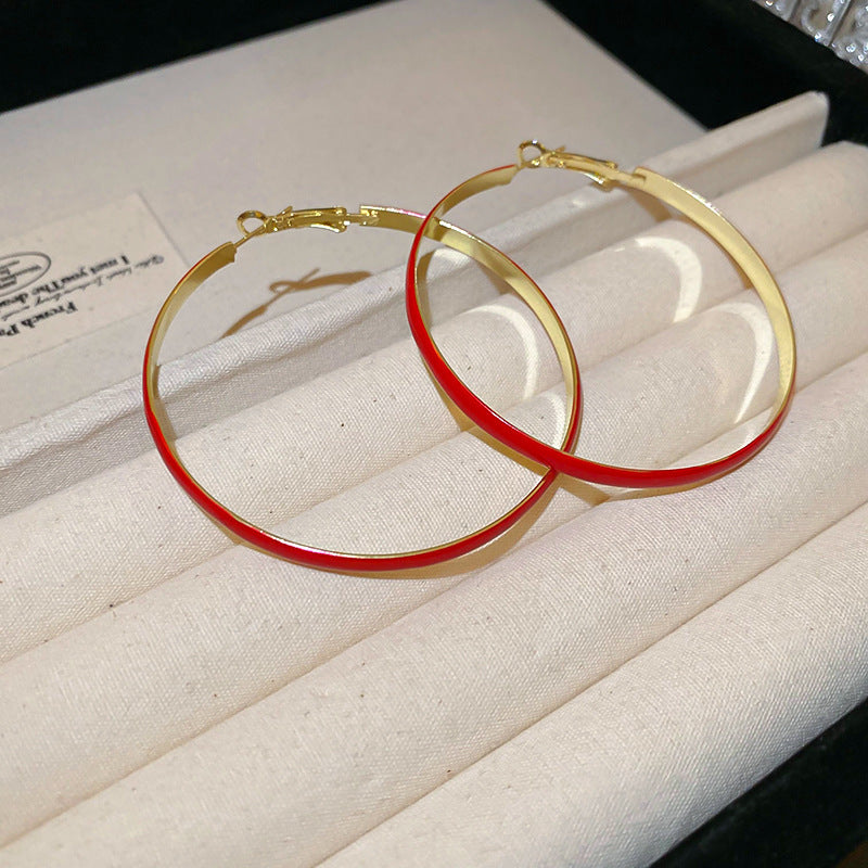 A pair of small gold hoop earrings with red enamel and decorative accents, placed on a white ceramic plate