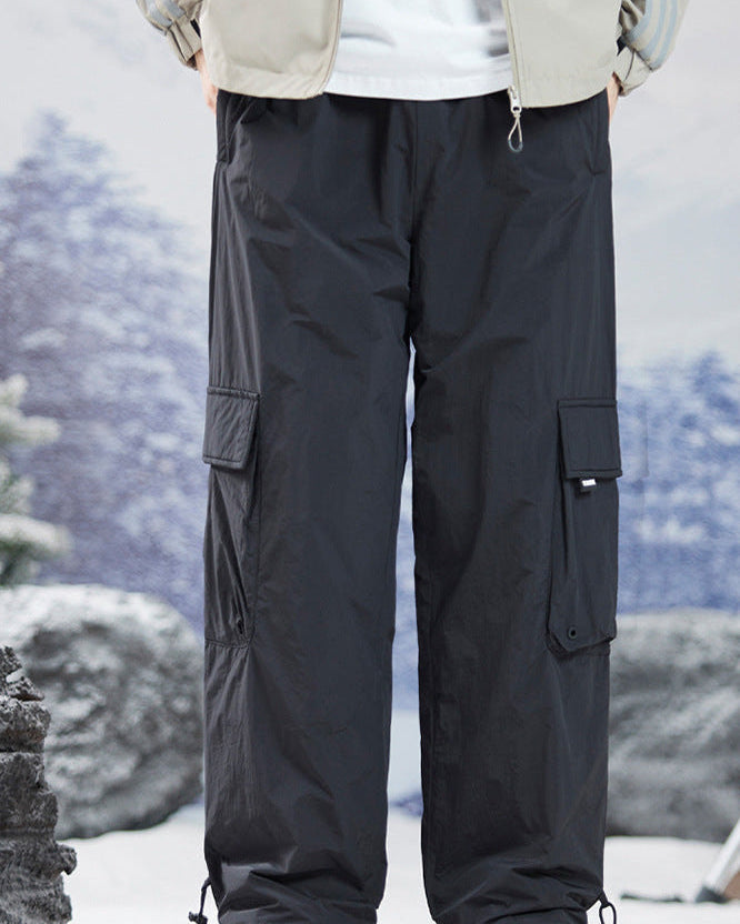 Black cargo pants with drawstring ankles shown against snowy mountain backdrop, featuring utility pockets and relaxed fit with hiking boots