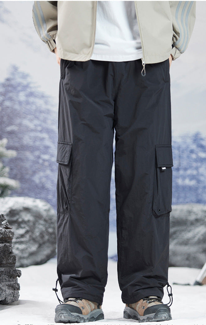 Black cargo pants with drawstring ankles shown against snowy mountain backdrop, featuring utility pockets and relaxed fit with hiking boots