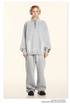 Model with blonde braids wearing light gray half-zip pullover and matching sweatpants, headphones, cream background