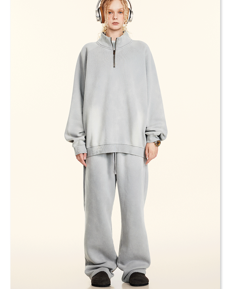 Model with blonde braids wearing light gray half-zip pullover and matching sweatpants, headphones, cream background