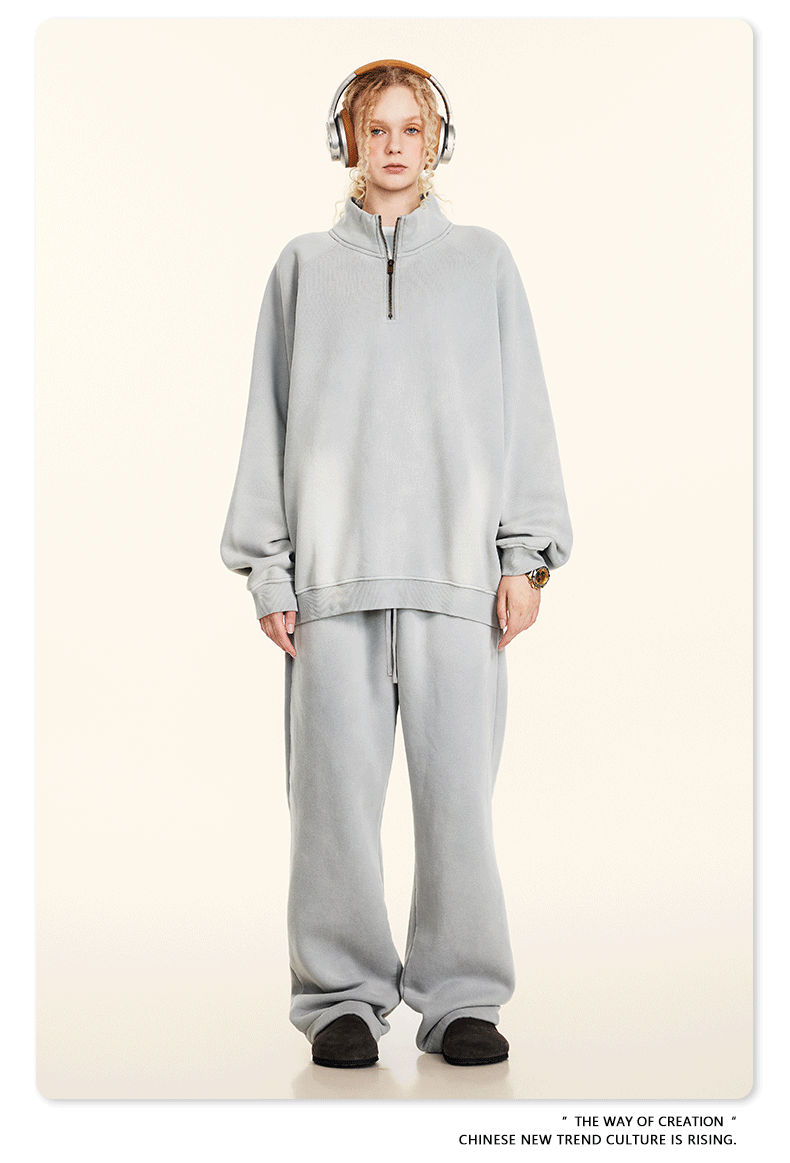 Model with blonde braids wearing light gray half-zip pullover and matching sweatpants, headphones, cream background