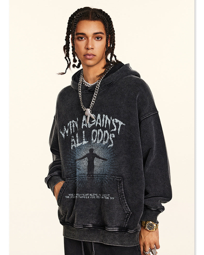 Model with braided hair wearing black "Win Against All Odds" graphic hoodie, standing in studio with chain necklace