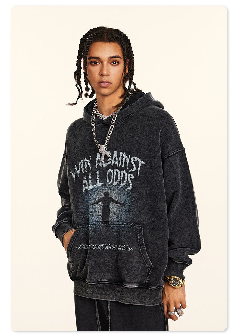 Model with braided hair wearing black "Win Against All Odds" graphic hoodie, standing in studio with chain necklace