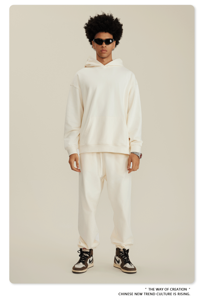 Man with afro wearing cream-colored hoodie and matching pants with black sunglasses and brown sneakers