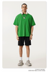 Model wearing bright green oversized t-shirt with white headphones around neck, styled with black shorts and chunky gray sneakers against white backdrop