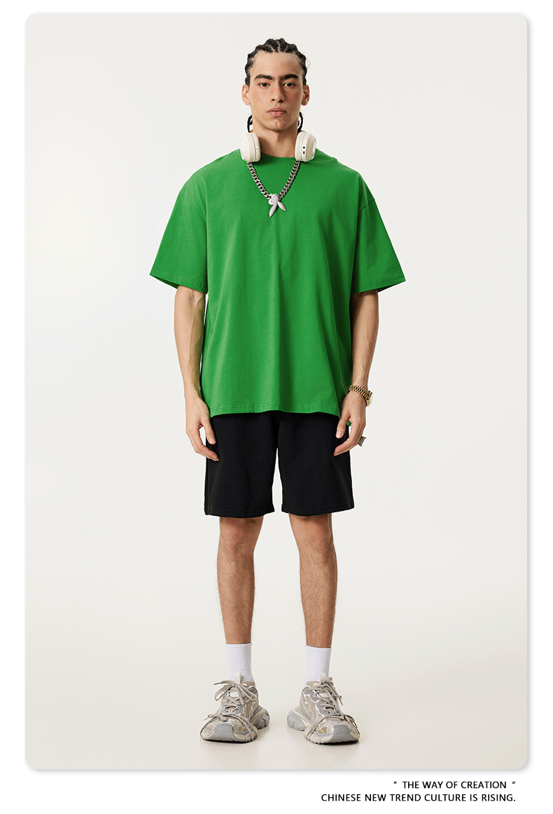Model wearing bright green oversized t-shirt with white headphones around neck, styled with black shorts and chunky gray sneakers against white backdrop