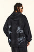 Rear view of model with twisted braids wearing black hoodie featuring graffiti designs and white painted symbols