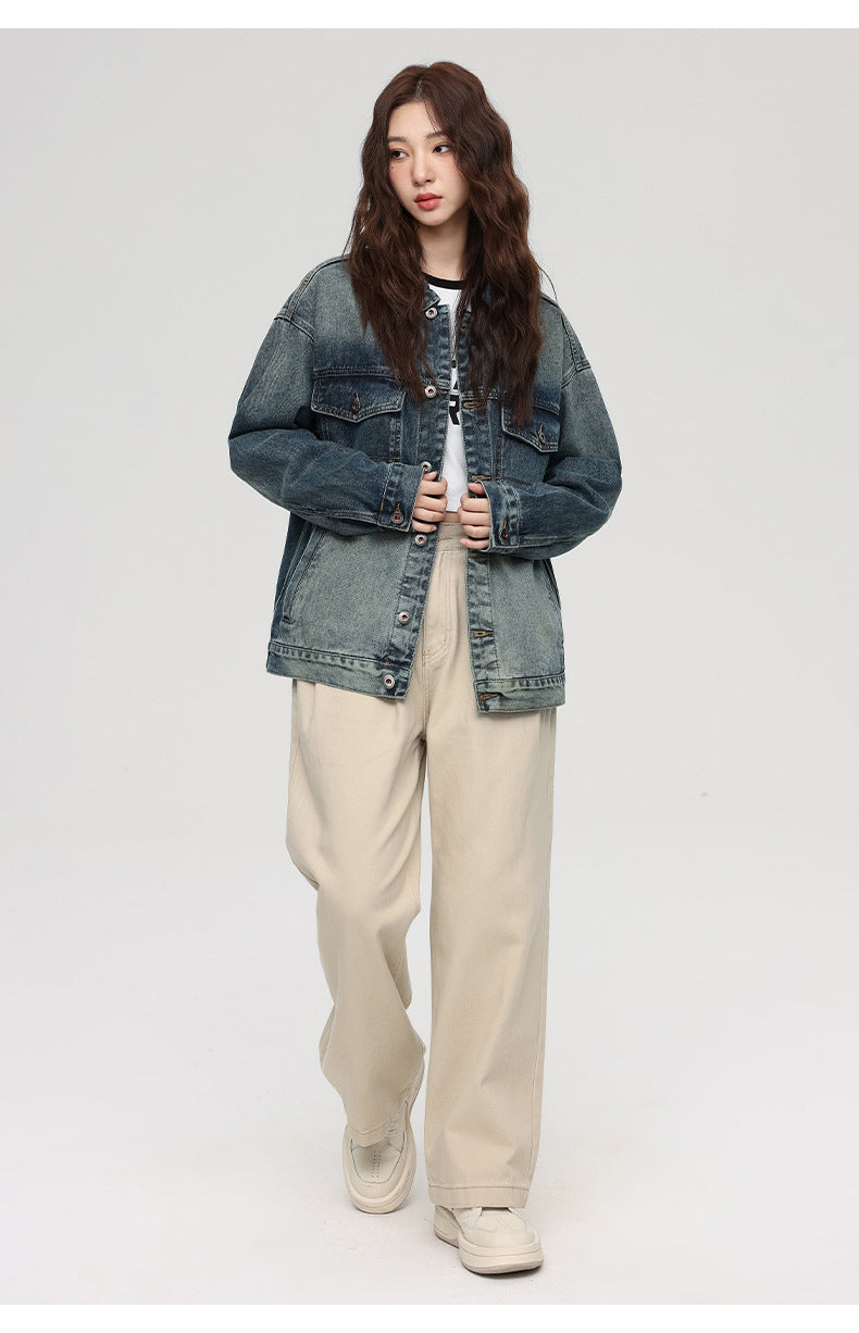 A woman is posing with hands at sides against a gray backdrop. Wearing gradient-wash denim jacket, white crop top and beige wide-leg pants