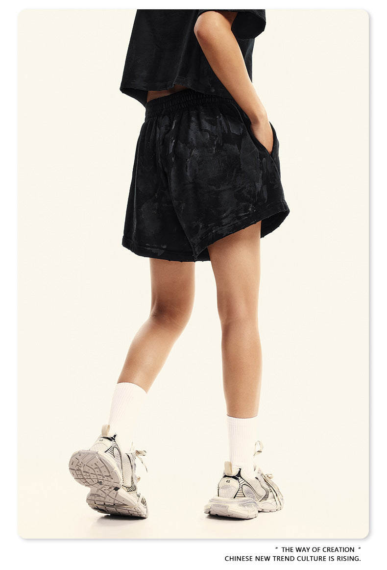 Side view of black washed shorts with elastic waistband, paired with white socks and chunky sneakers