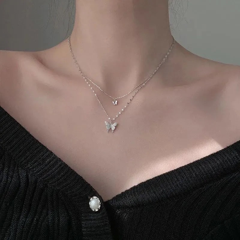 Sterling silver layered necklace with small butterfly charm and crystal butterfly pendant worn with black top