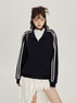 A woman wearing a navy zip-up jacket with white side stripes, white top, black choker, and white lace skirt stands against neutral background