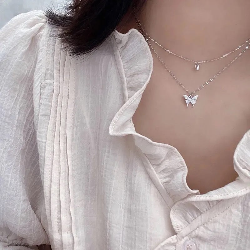 Layered butterfly pendant necklace styled with white ruffled cotton blouse