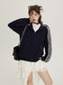 A woman touching her face while modeling a navy sporty jacket with white stripes, paired with white lace skirt and black chain shoulder bag