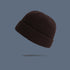 A dark brown ribbed knit beanie with folded cuff floating against slate gray background, showing classic winter hat texture