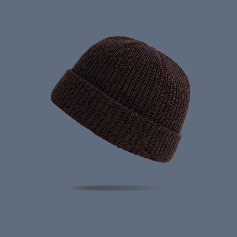 A dark brown ribbed knit beanie with folded cuff floating against slate gray background, showing classic winter hat texture