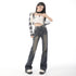 A woman wearing high-waisted faded black wide-leg jeans, a white and black patterned crop top, and chunky platform shoes, posing with one hand on her hip