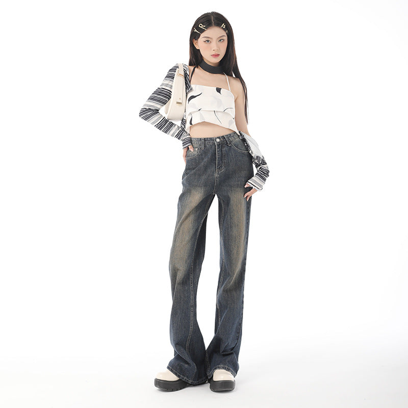 A woman in vintage-wash black denim wide-leg jeans, a monochrome abstract crop top, and chunky sneakers, posing with a tilted stance