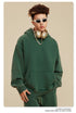 Man in green pullover hoodie with gold headphones and chunky white necklace against neutral background
