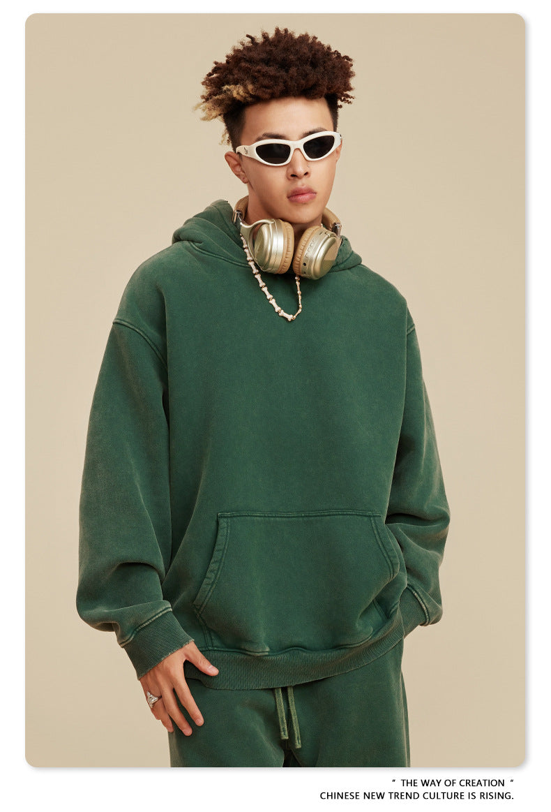 Man in green pullover hoodie with gold headphones and chunky white necklace against neutral background