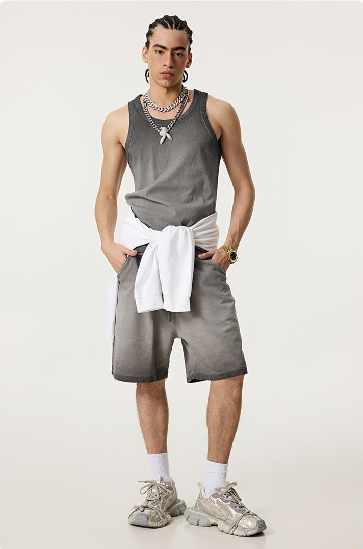 Male model wearing a gray ombre tank top and matching shorts, with a white sweater tied at the waist and silver accessories