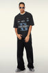 A model posing in black graphic t-shirt with blue 'B' logo design, silver chain necklace, white sunglasses and black wide-leg pants