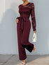 A dynamic pose in the burgundy lace jumpsuit, highlighting the delicate lace detailing and flowing pant legs.