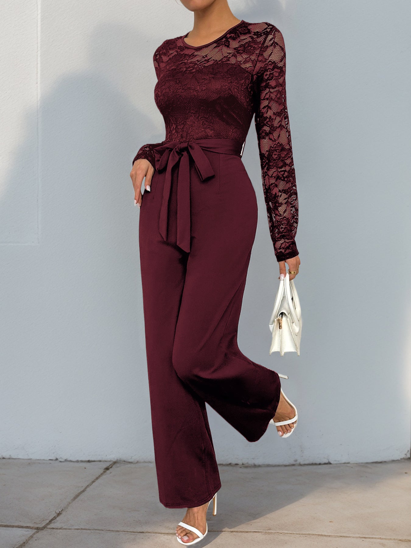 A dynamic pose in the burgundy lace jumpsuit, highlighting the delicate lace detailing and flowing pant legs.