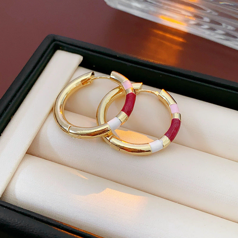 A pair of triangular gold stud earrings with red enamel and clear baguette-cut gemstones, displayed on a fabric-lined jewelry tray