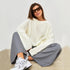 Woman in white oversized sweater with sunglasses, wearing grey pants and white sneakers