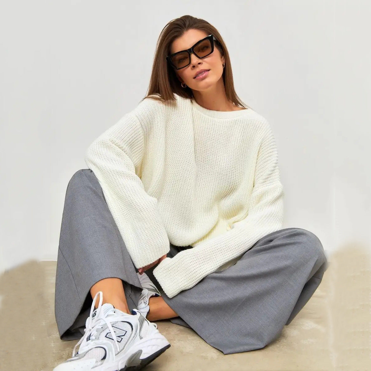 Woman in white oversized sweater with sunglasses, wearing grey pants and white sneakers
